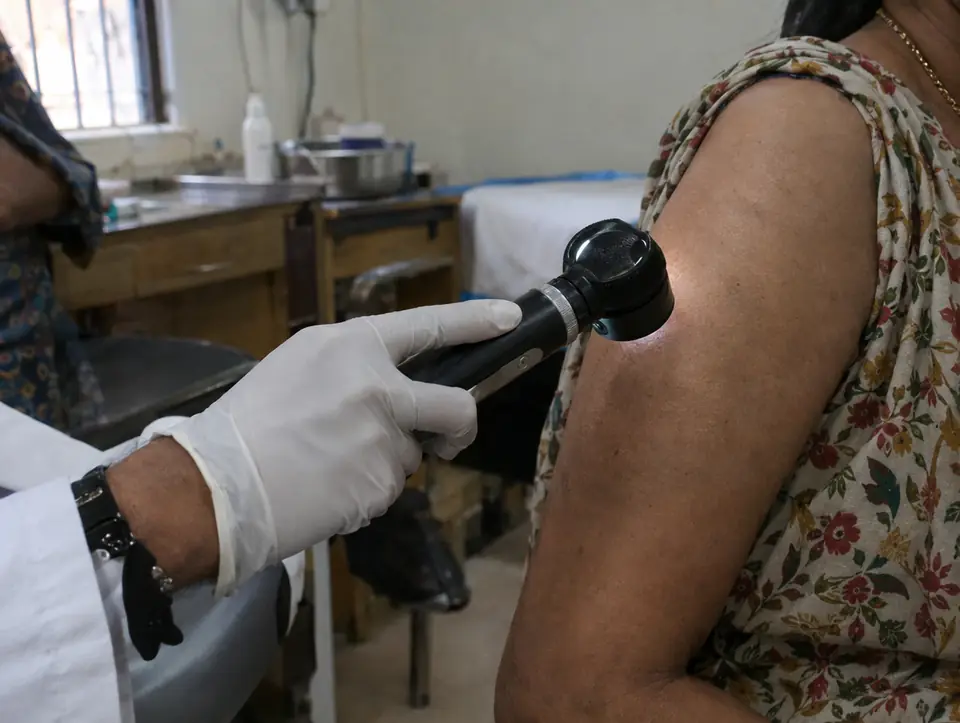 A doctor's gloved hand holding a handheld dermatoscope against the skin of a patient's upper arm
