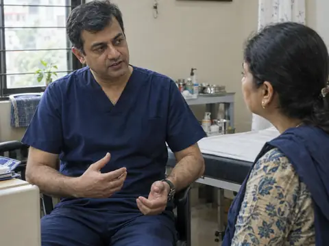 An Indian male surgeon in his forties in navy scrubs talking with an Indian woman patient in an outpatient room before her procedure