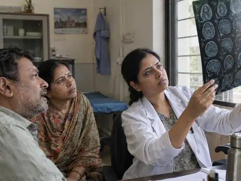 An Indian woman neurosurgeon reviewing a brain MRI film held up to a window with an Indian man patient and his wife