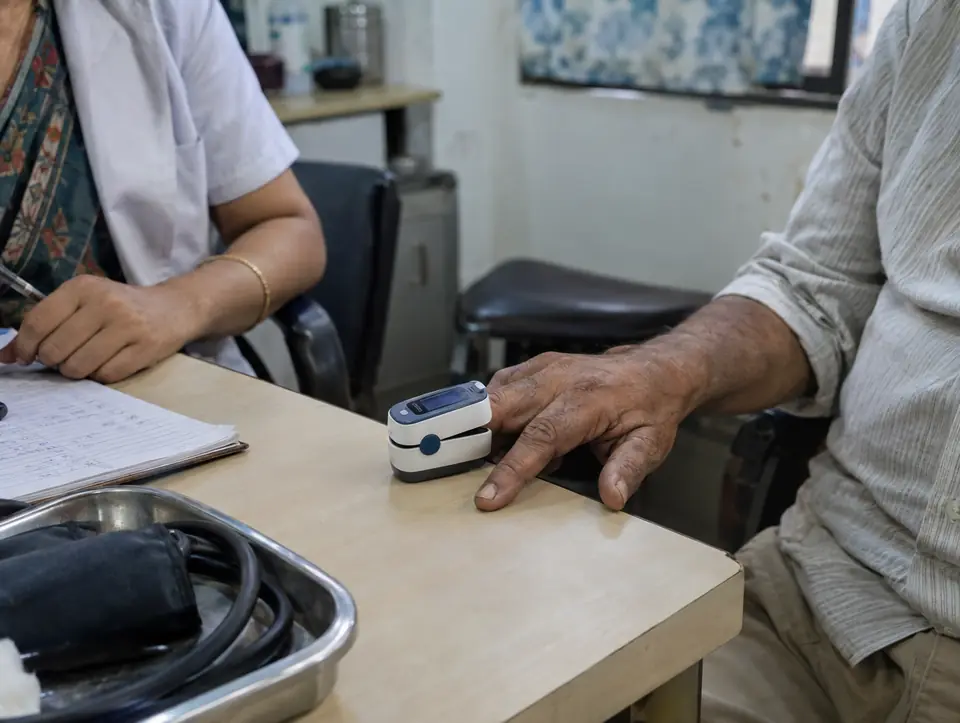 A fingertip pulse oximeter clipped on an older man's finger, the hand resting on a clinic desk